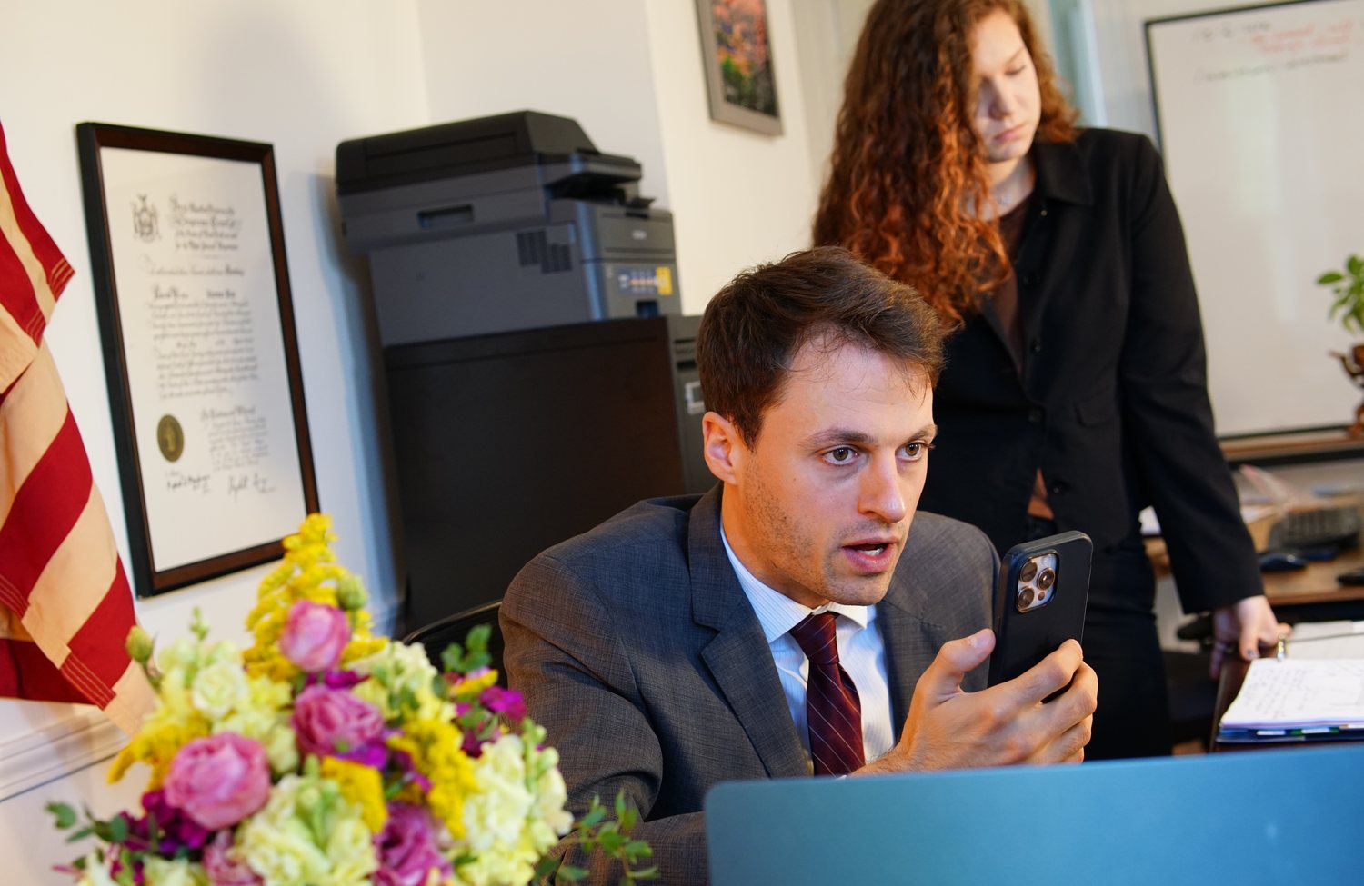 Thomas Plan at his desk on the phone, with his paralegal Leah standing beside him.